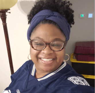 Woman wearing glasses, smiling in front of wall