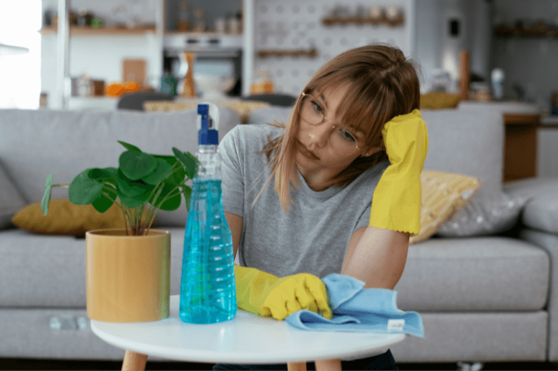 Woman wearing cleaning gloves looking exhausted while surrounded by household chemical cleaning products